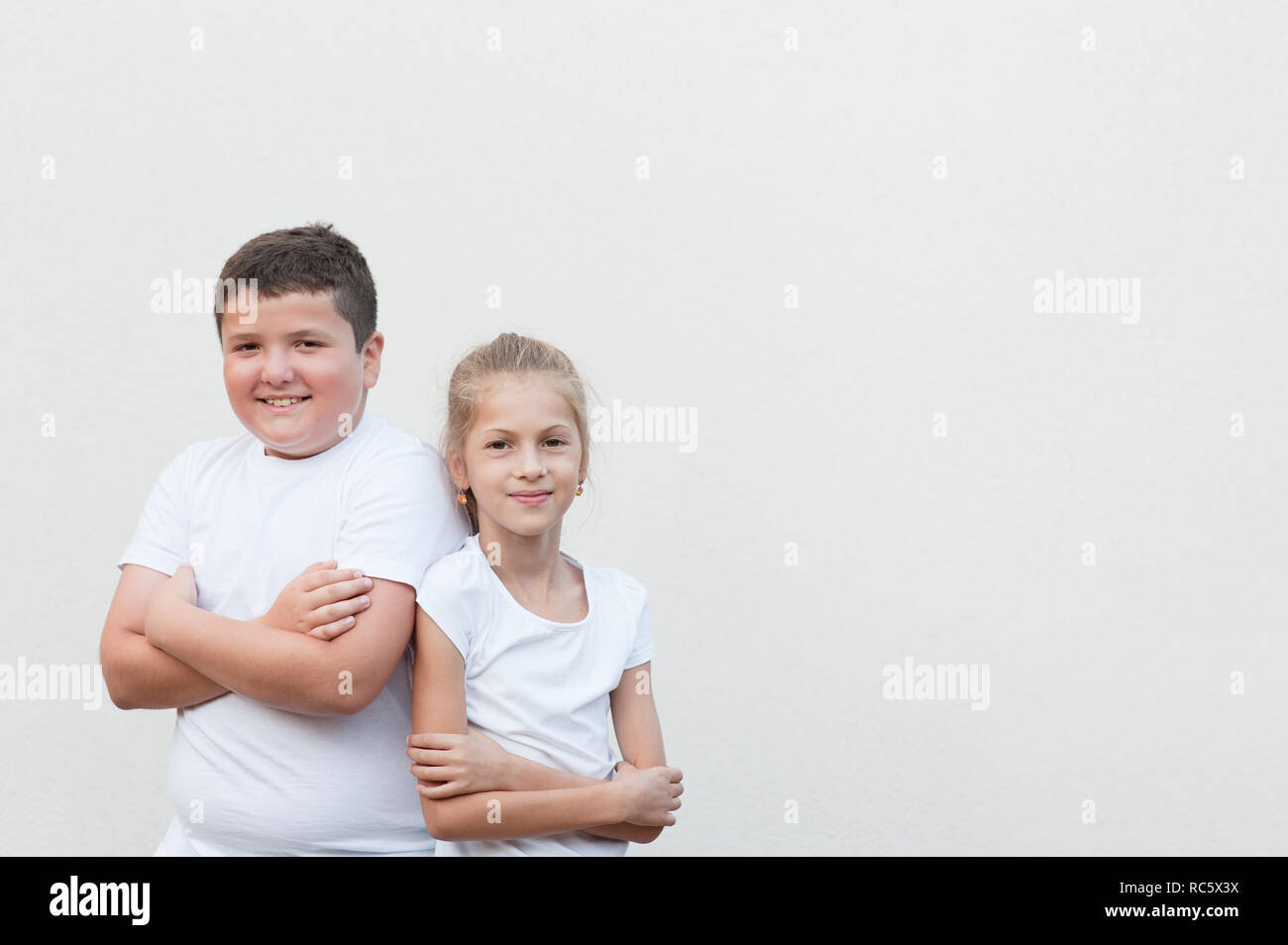 happy cute thick young boy shoulder to shoulder with very thin little pretty girl in white shirt with copyspace Stock Photo