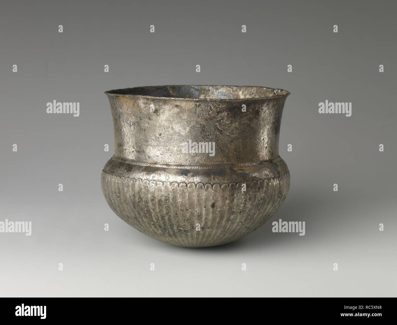 Bowl with flutes from shoulder to rosette at base and with inscribed weight. Dimensions: H. 10.5 x Diam. 12 cm at mouth, 13 at body (4 1/8 x 4 3/4 and 5 1/8 in). Date: 4th century B.C..  The heavy silver vessels 18.2.13-18.2.17 are in created in a decorative style widespread in the Greek world, and can be dated to the fourth century BC. They. are said to have been found together in the Egyptian Delta.   Several of the vessels have small Demotic designations scored into the rim recording the weight of the silver, which correlated with the vessel's value. The larger weight unit was a deben (abou Stock Photo