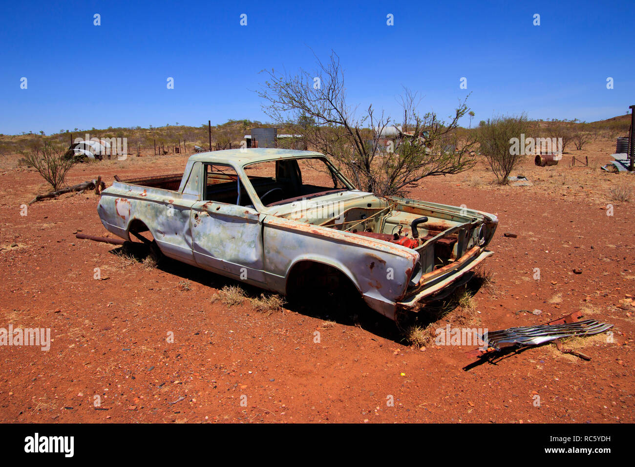An old pick up truck utility lies abandoned in the Australian outback with blue sky and red soil. Stock Photo