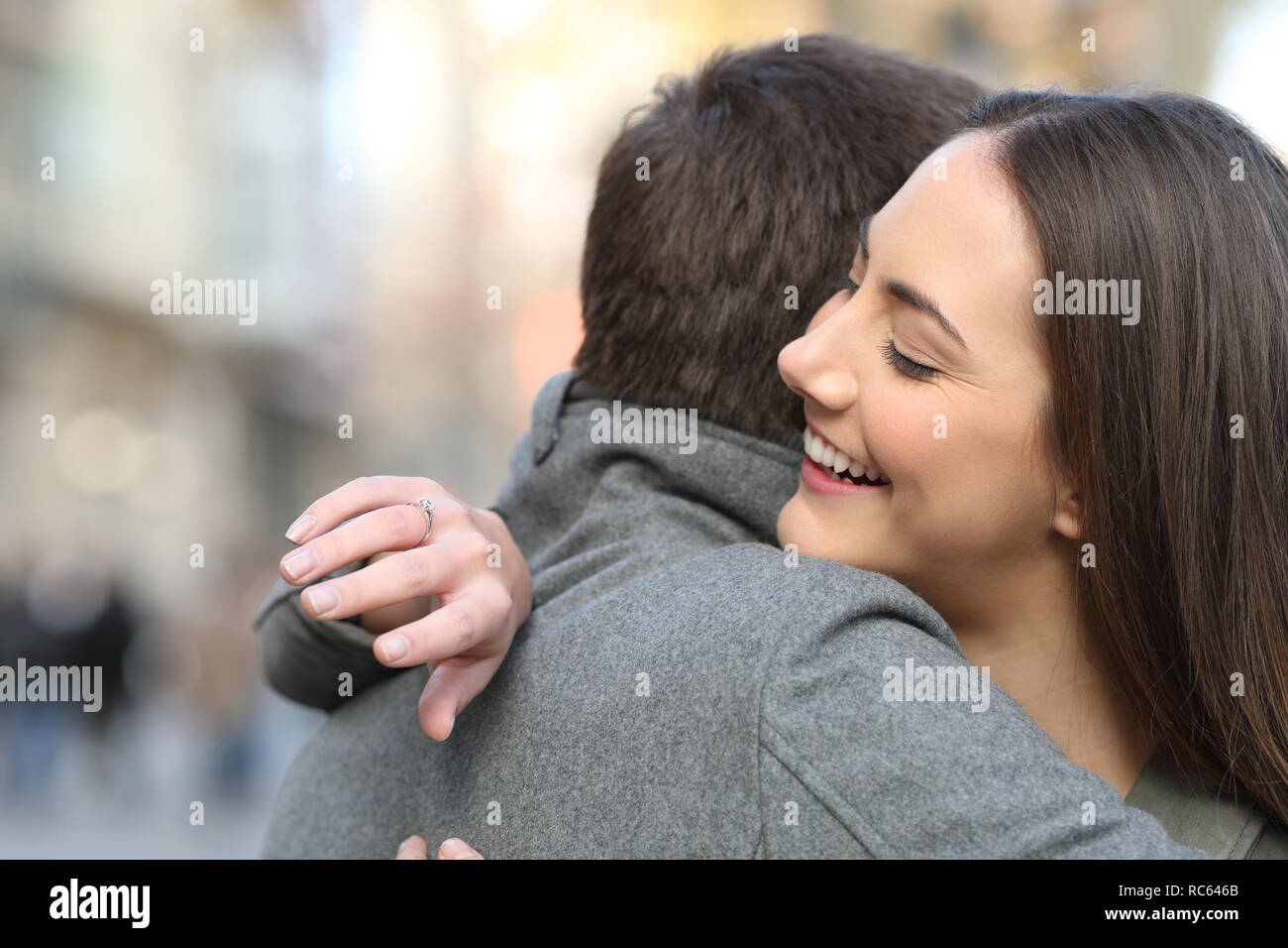 Couple hugging after marriage proposal and girlfriend looking at engagement ring in the street Stock Photo