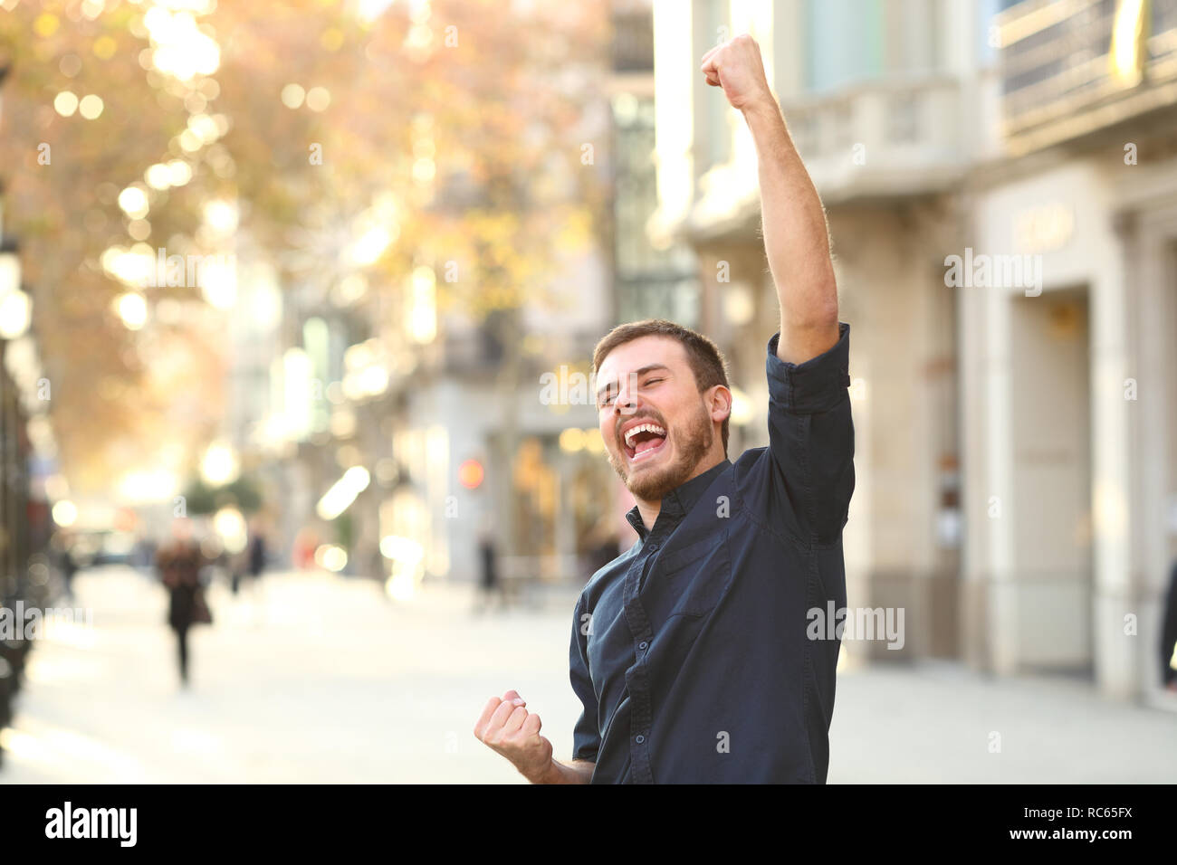 Excited man raising arms celebrating sucess in the middle of the street Stock Photo