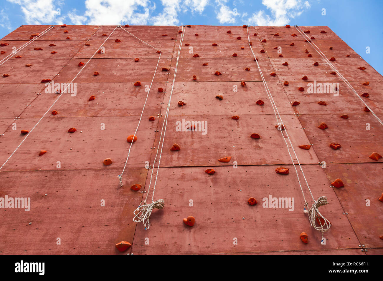 Artificial rock climbing wall with grips for hands and feet in outdoor adventure park used to practise lead climbing or bouldering Stock Photo