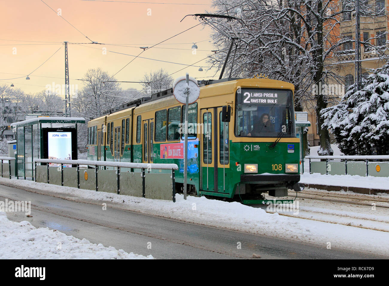 Helsinki, Finland - January 9, 2019: Green HSL tram No. 2 departs from tram stop on a beautiful day of winter with snowfall in Helsinki. Stock Photo
