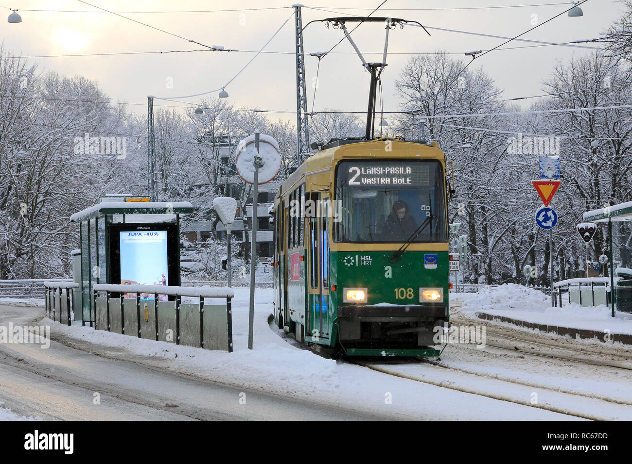 Helsinki, Finland - January 9, 2019: Green HSL tram No. 2 on a tram stop on a day of winter with light snowfall in Helsinki. Stock Photo