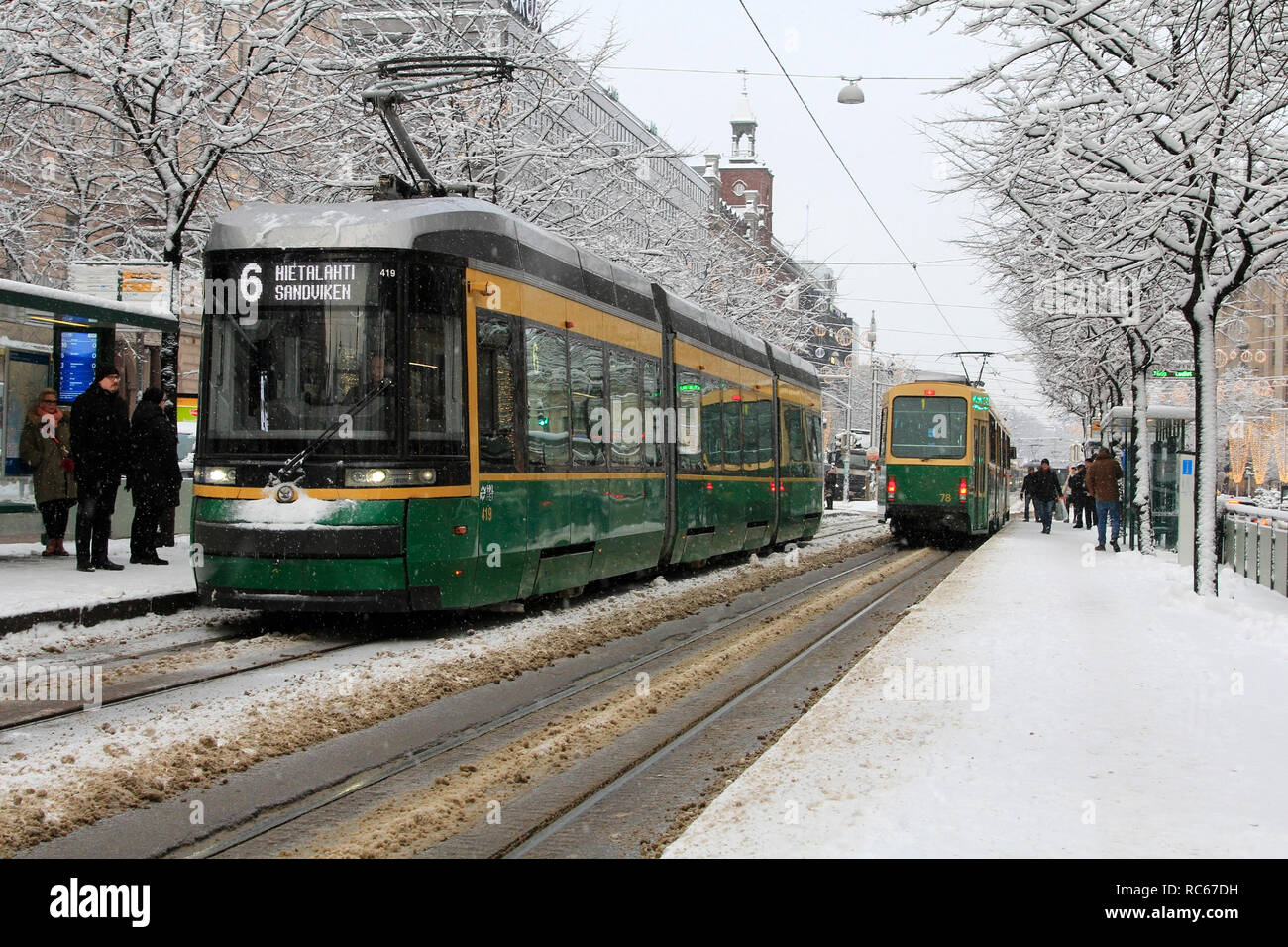 Helsinki, Finland - January 9, 2019: People get on green HSL trams on a tram stop in Helsinki city centre on a day of winter snowfall. Stock Photo
