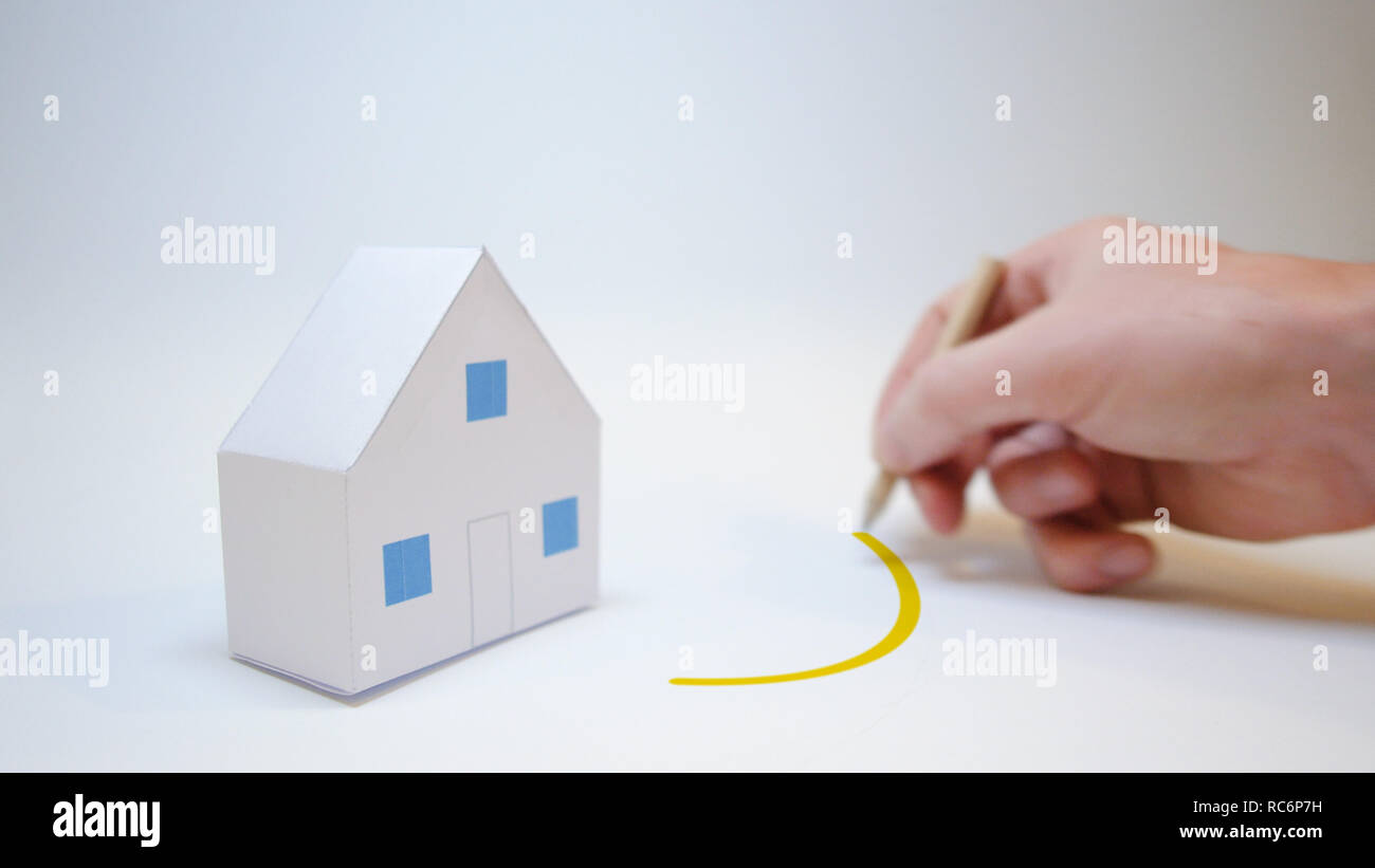 hand draws a yellow circle next to a paper house purchase home symbol Stock Photo