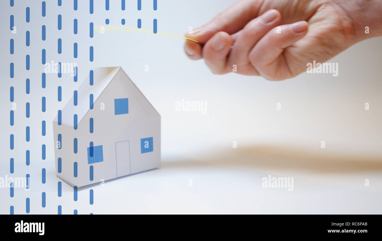 an insurer's hand protects a paper house from natural disasters Stock Photo