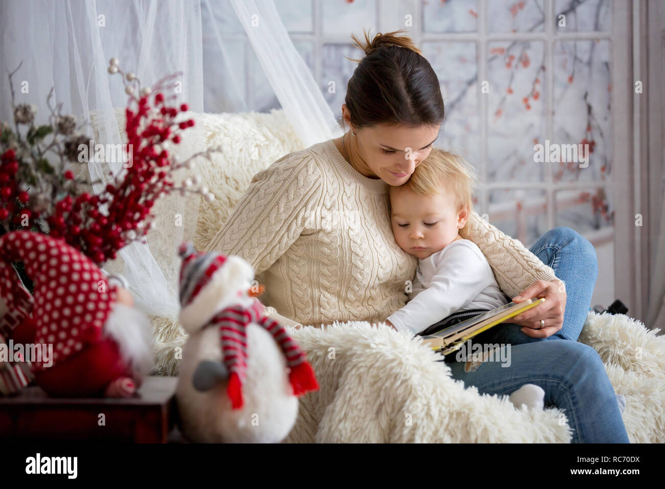 Mother breastfeeding her toddler son sitting in cozy armchair, snowing outside wintertime Stock Photo
