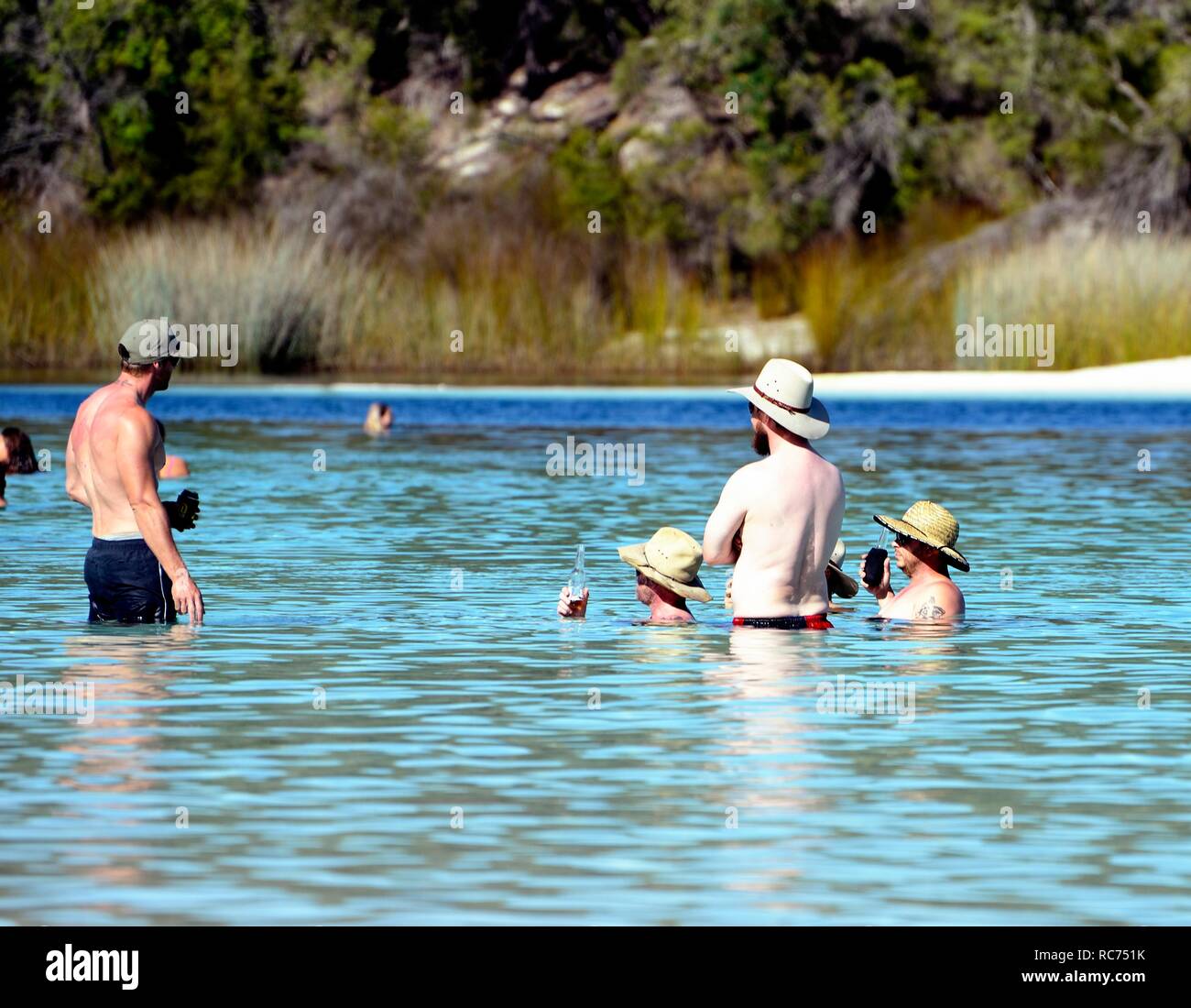Four Australian men sit drinking beer and talking in Lake Mckenzie, Fraser Island, Australia Stock Photo