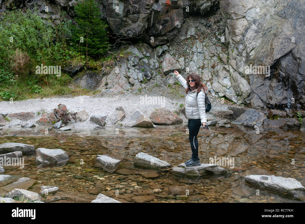 Woman skips over stepping stones placed in a pond. Photographed on the 'Wild Water Way' Stubai, Tyrol, Austria Stock Photo