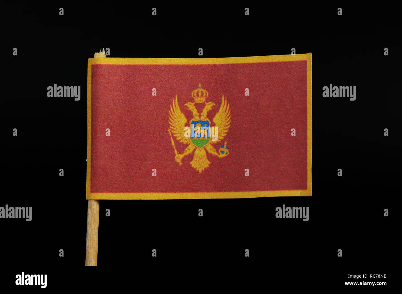 A official and national flag of Montenegro on toothpick on black background. A red field surrounded by a golden border; charged with the Coat of Arms  Stock Photo