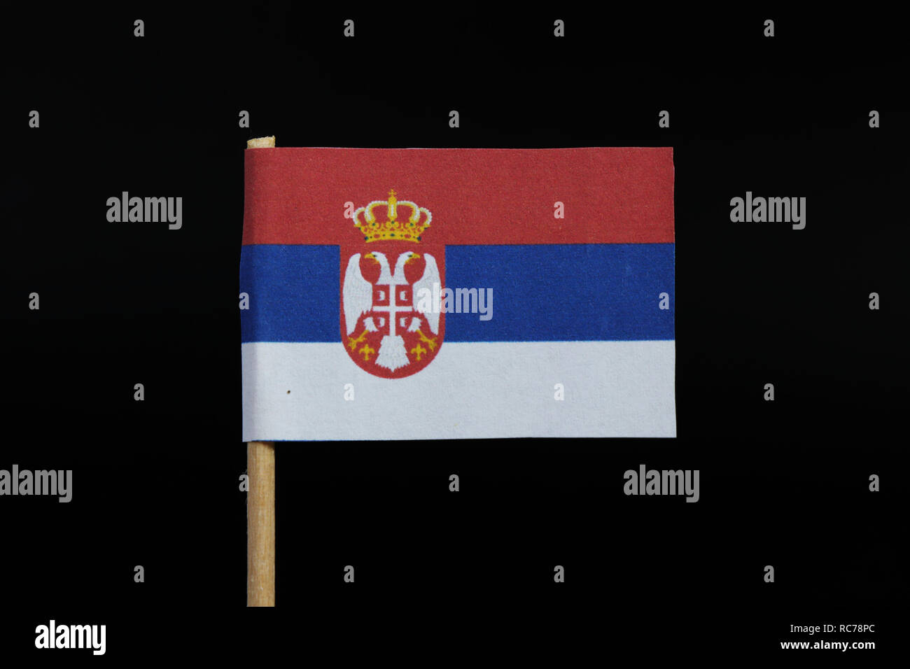 A national flag of Serbia on toothpick on black background. A horizontal tricolor of red, blue, and white with coat of arms. Stock Photo