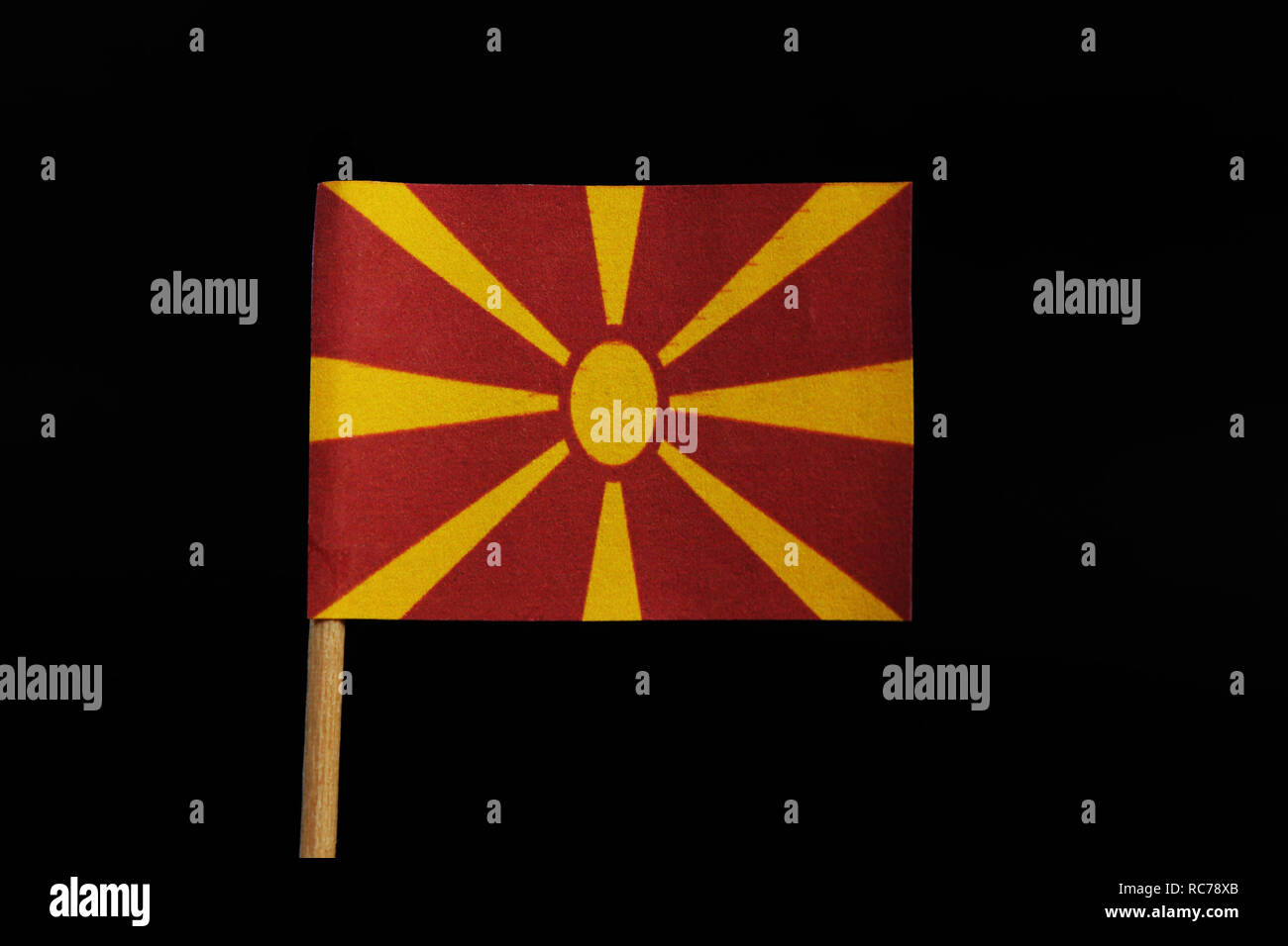 A unique and very original, national flag of the Republic of Macedonia on toothpick on black background. Stylised yellow sun on red field, with eight  Stock Photo