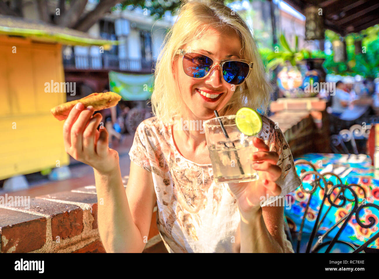 Happy caucasian woman drinks Margarita, Mexican cocktail based on tequila, and eats enchilada, a typical Mexican food. El Pueblo in Los Angeles Downtown State Historic Park, California, United States. Stock Photo