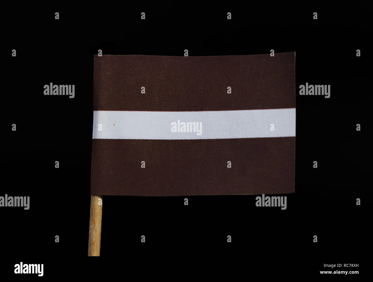 A unique and national flag of Latvia on toothpick on black background. A carmine field bisected by a narrow white stripe. Stock Photo