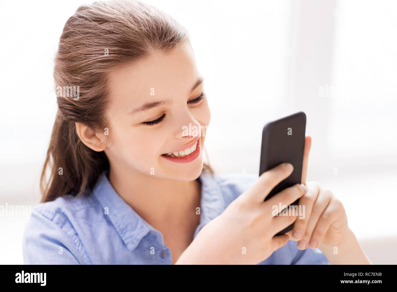 smiling girl messaging on smartphone at home Stock Photo