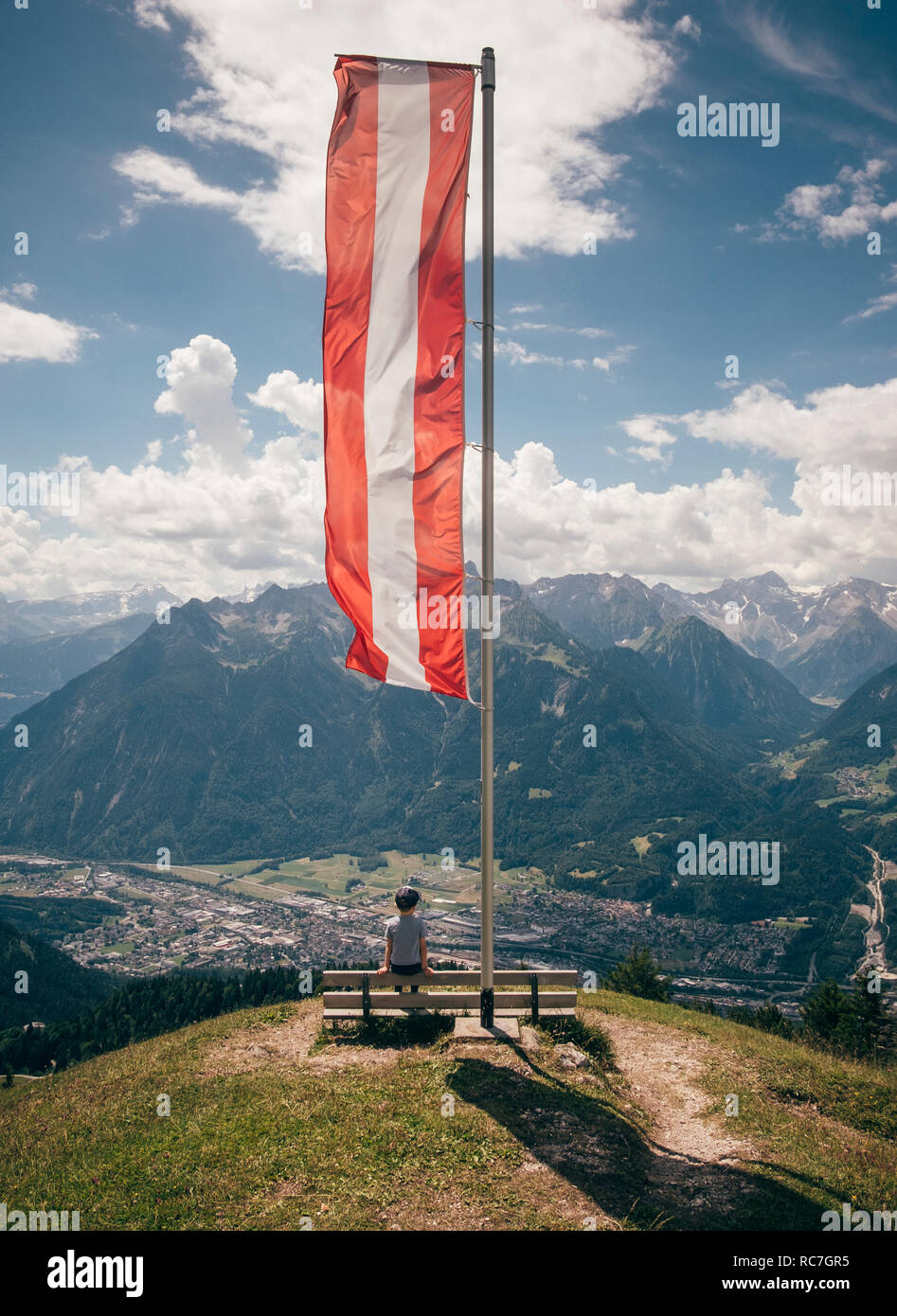 Boy sitting under Austrian flag contemplating mountain landscape, Bludenz, Vorarlberg, Austria Stock Photo