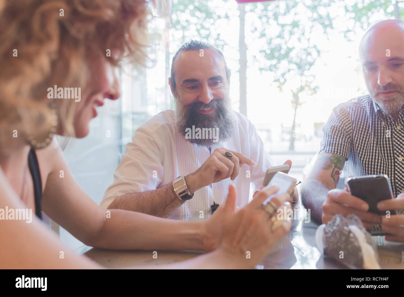 Mid adult woman and male friends looking at smartphones in cafe Stock Photo