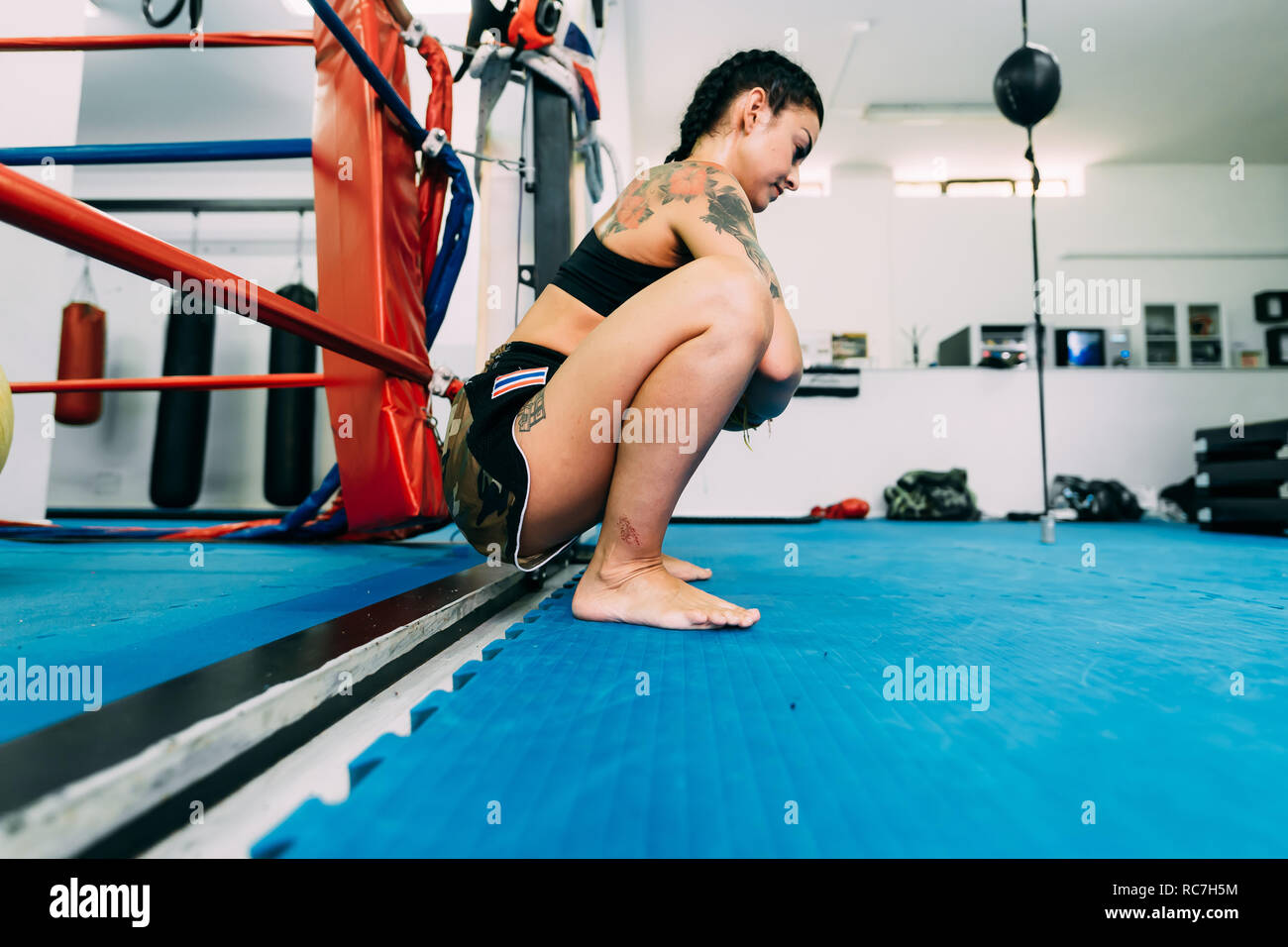 Female boxer squatting by boxing ring ropes Stock Photo