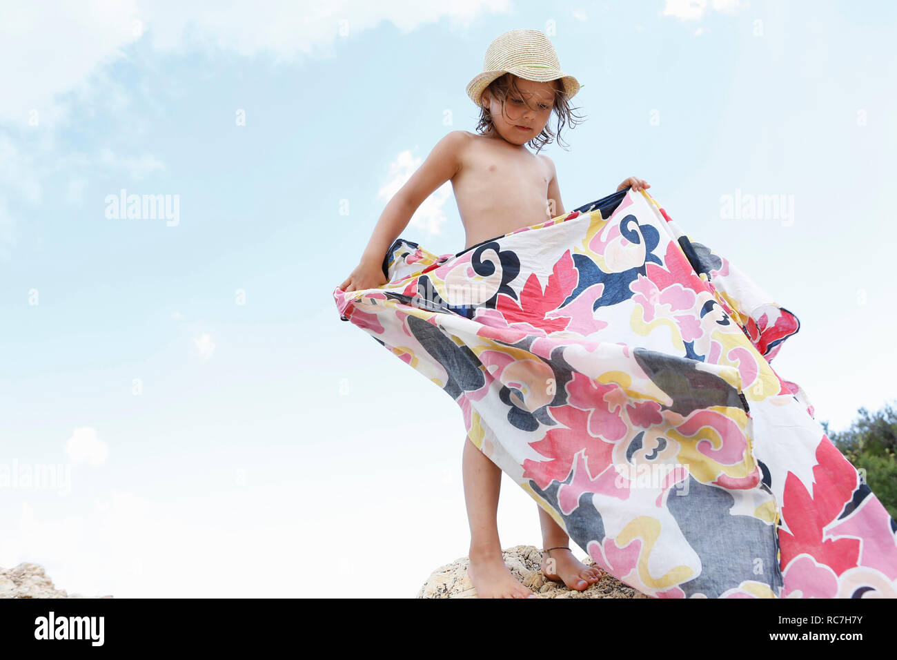 Girl standing on rock folding patterned blanket, Scopello, Sicily, Italy Stock Photo