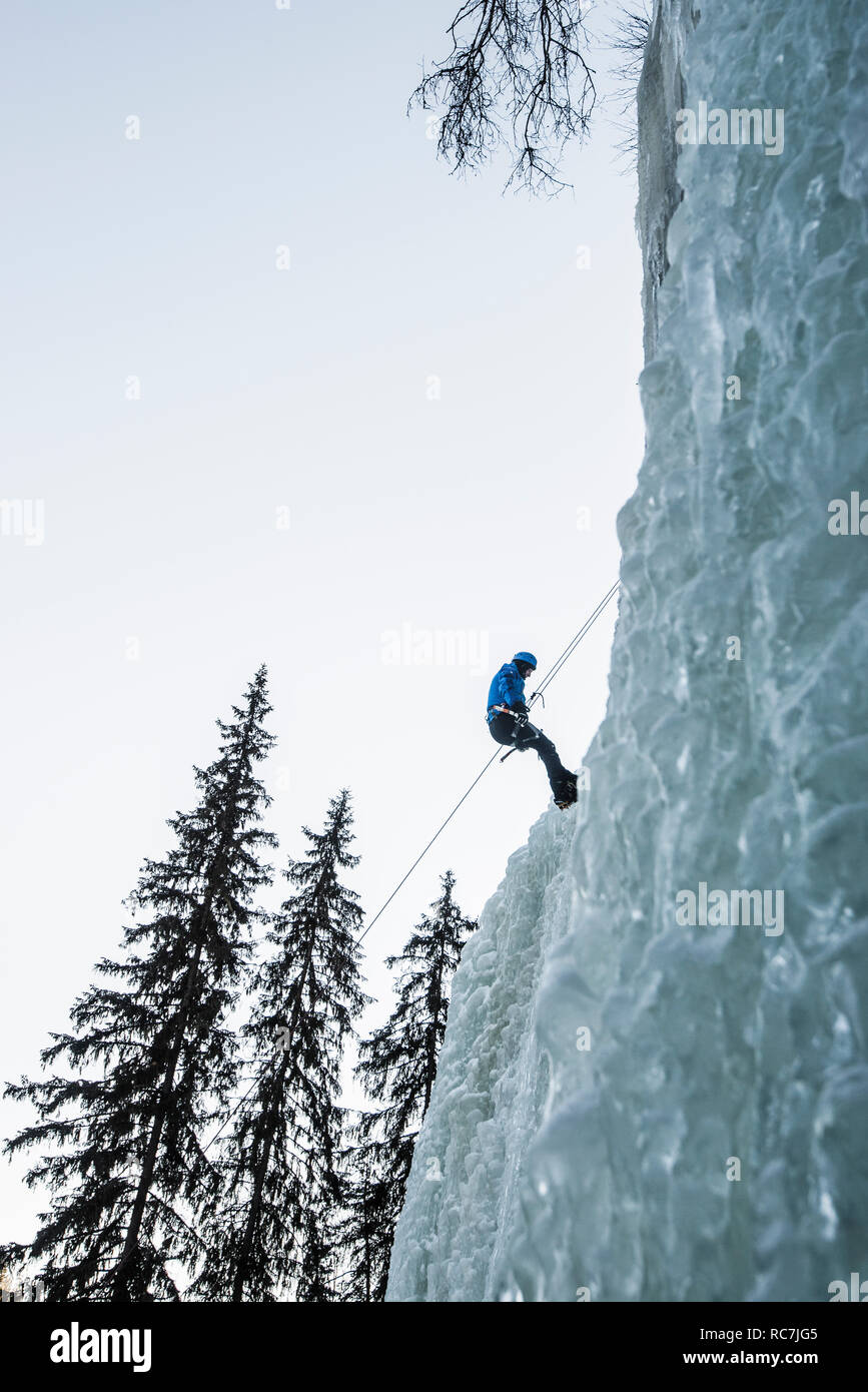Man climbing up with rope on frozen waterfall Stock Photo