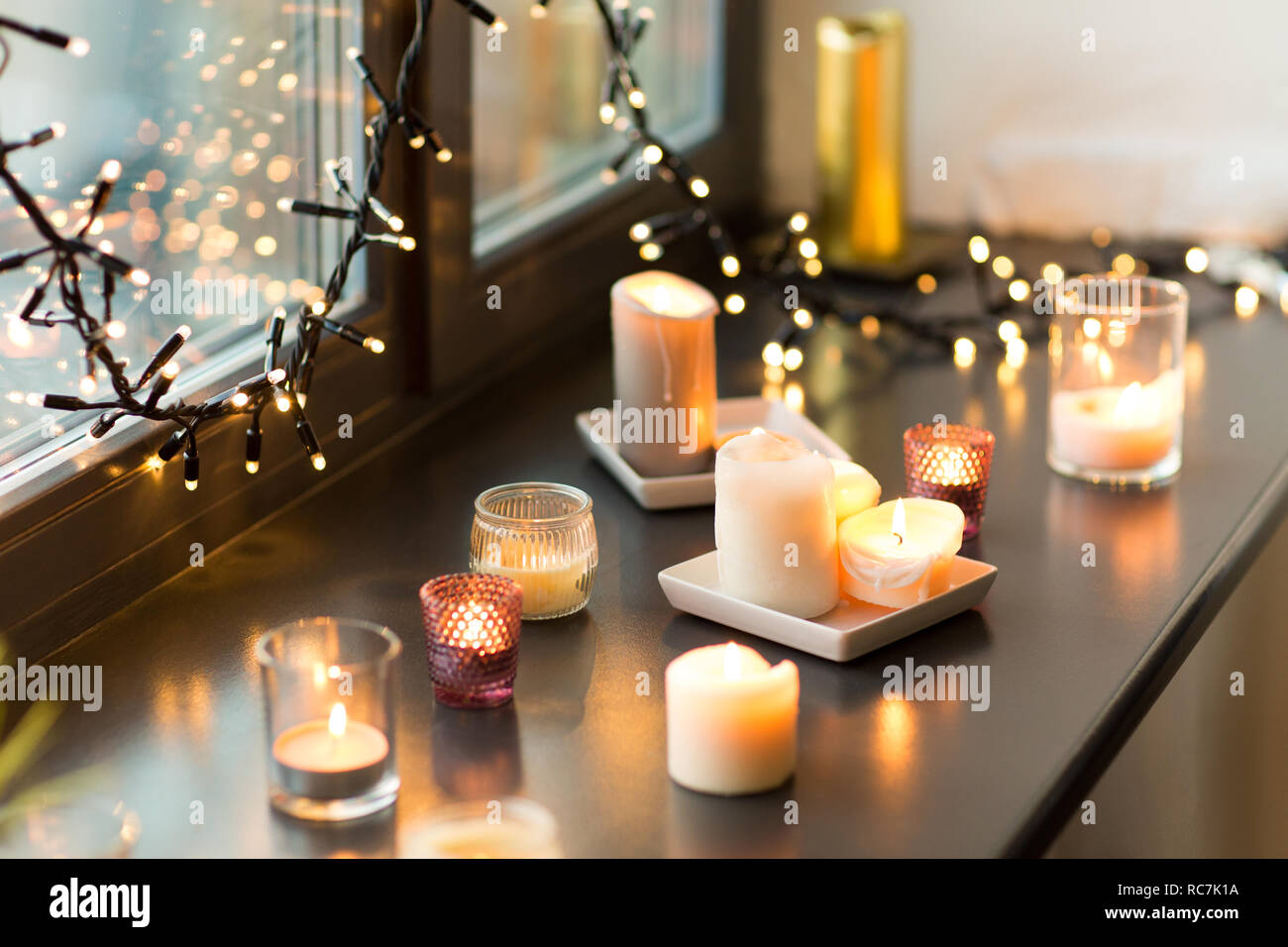 candles burning on window sill with garland lights Stock Photo Alamy