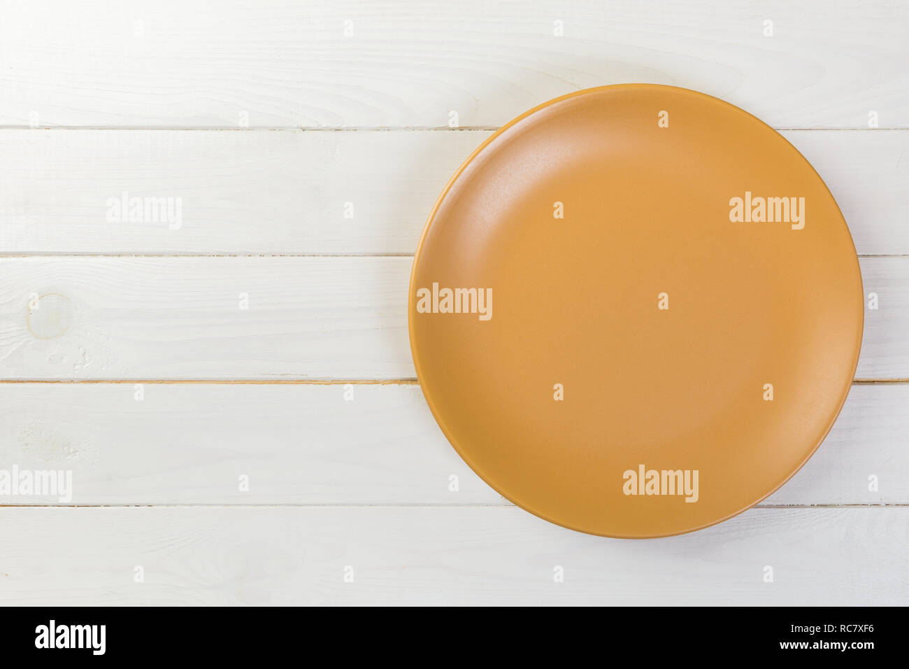 Directy above Empty yellow matte plate on white wooden background with ...
