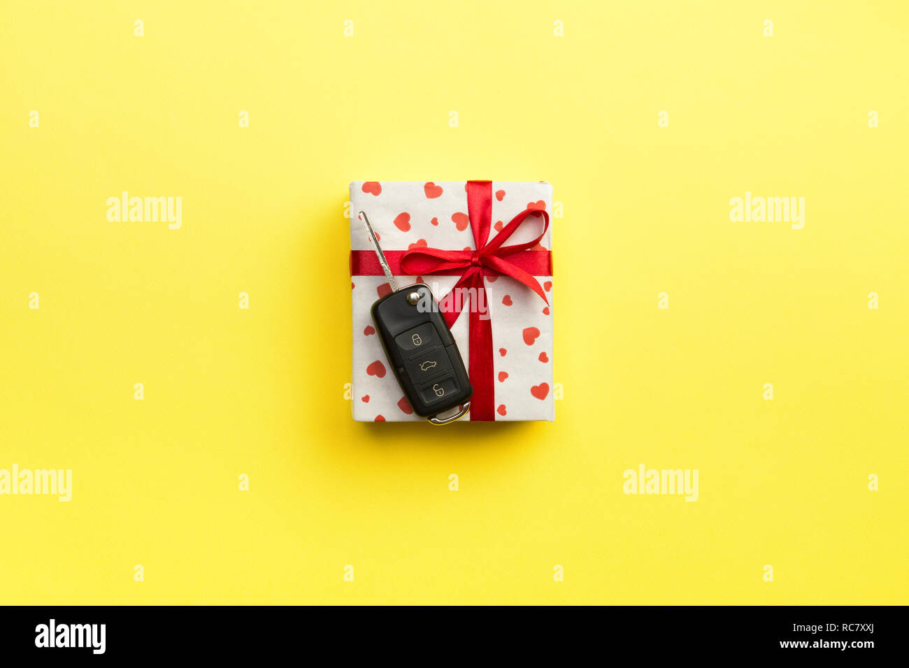 Car key on paper gift box with red ribbon bow and heart on yellow table ...
