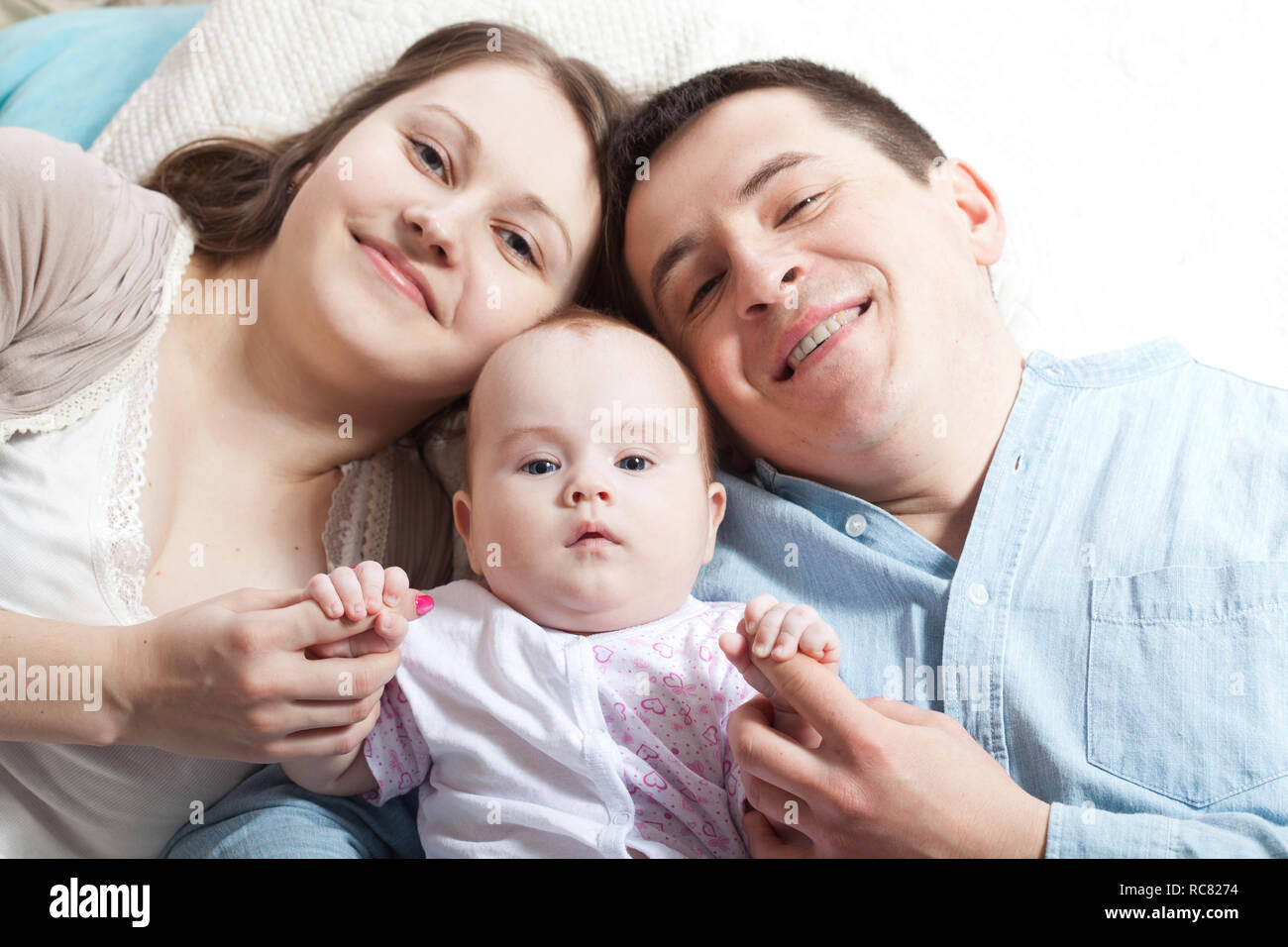 Family concept - baby with dad and mom. Portrait of happy young parents with baby in the bed at home. Stock Photo