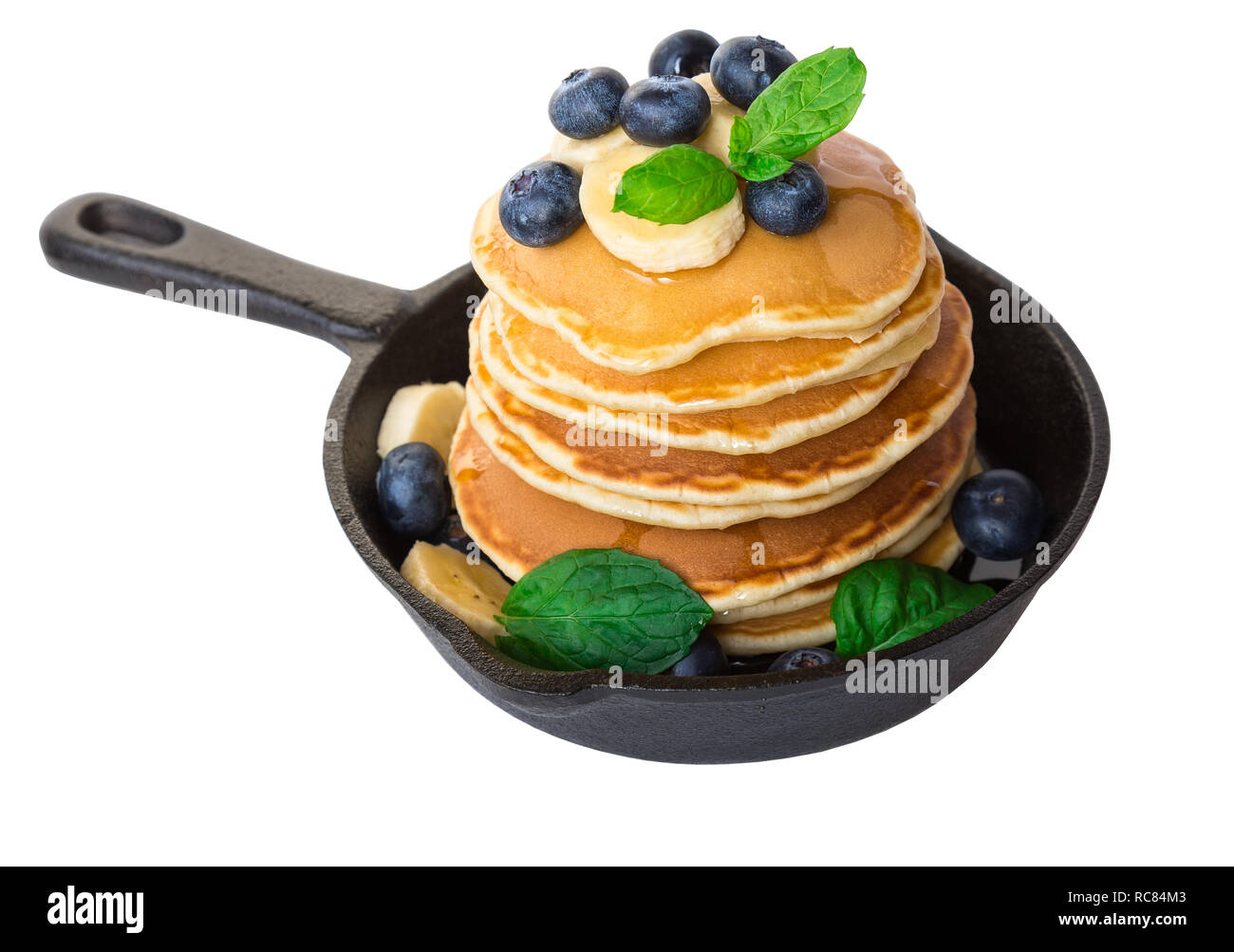 Stack of homemade pancakes in iron skillet with blueberries, banana and mint leaves isolated on white background. Stock Photo