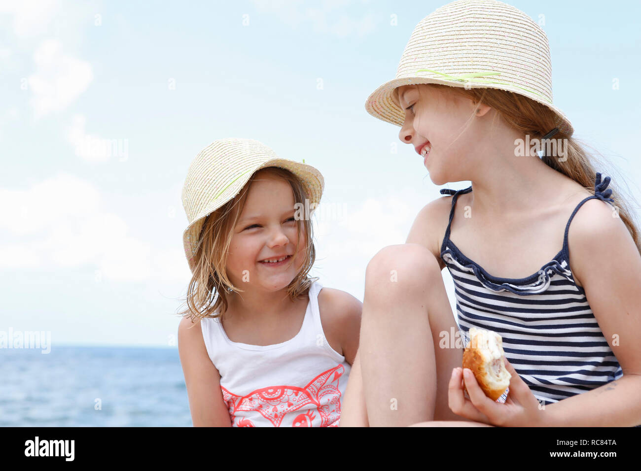 Two girls in sun hats eating sandwiches on beach, Scopello, Sicily, Italy Stock Photo