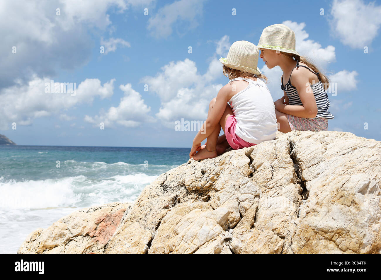 Two girls looking out at sea from rock, Scopello, Sicily, Italy Stock Photo