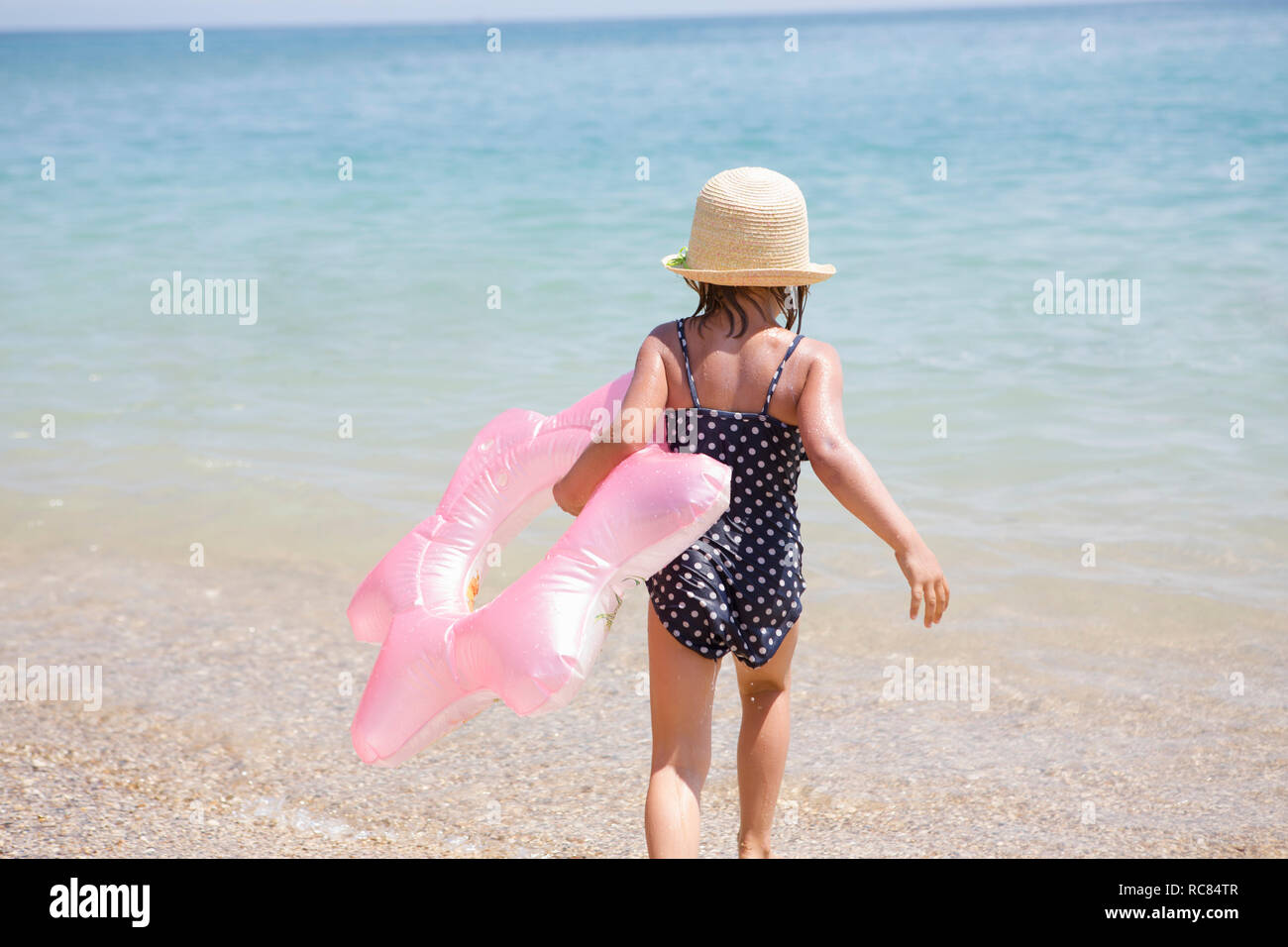 Girl carrying pink inflatable into sea, Scopello, Sicily, Italy Stock Photo