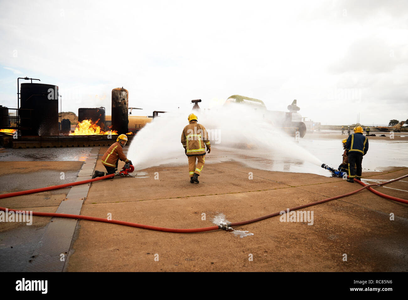 Firemen training, spraying water onto fire at training facility Stock Photo