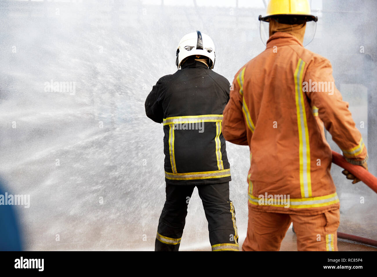 Firemen training, firemen spraying water at training facility, rear view Stock Photo