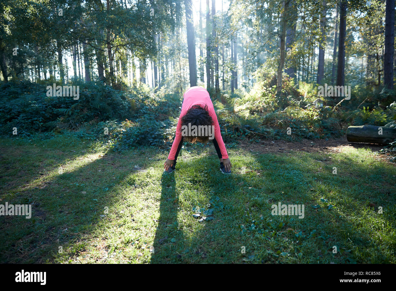 Young female bending forward stretching in forest Stock Photo