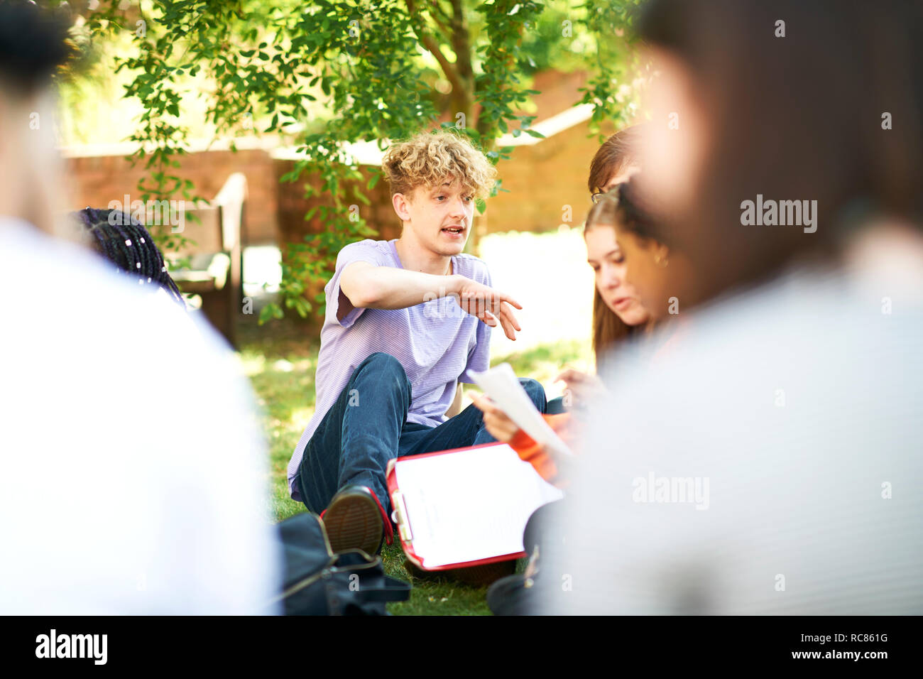 Male and female higher education students discussing paperwork on college campus lawn, over shoulder view Stock Photo