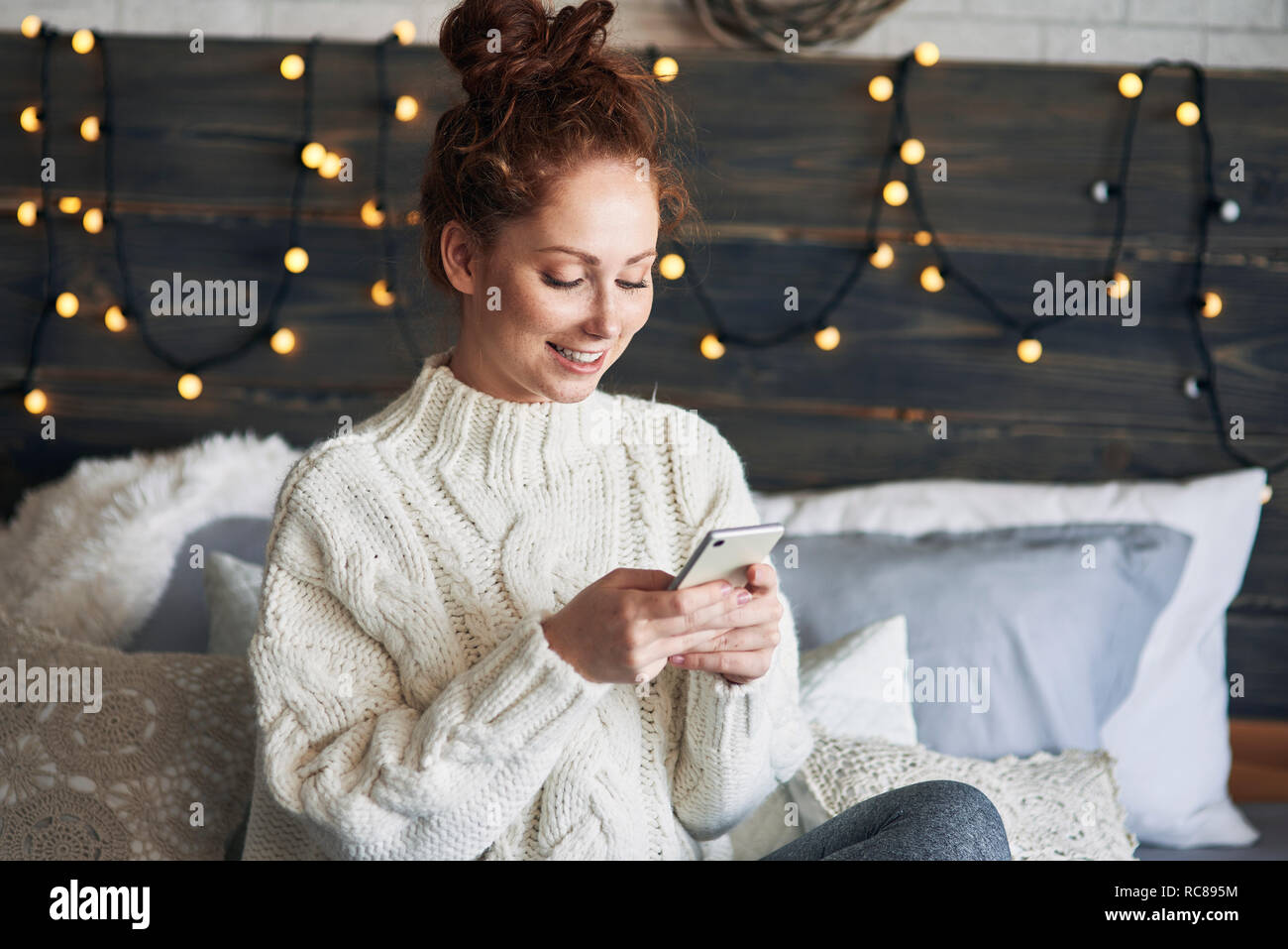 Woman texting on bed decorated with Christmas lights Stock Photo
