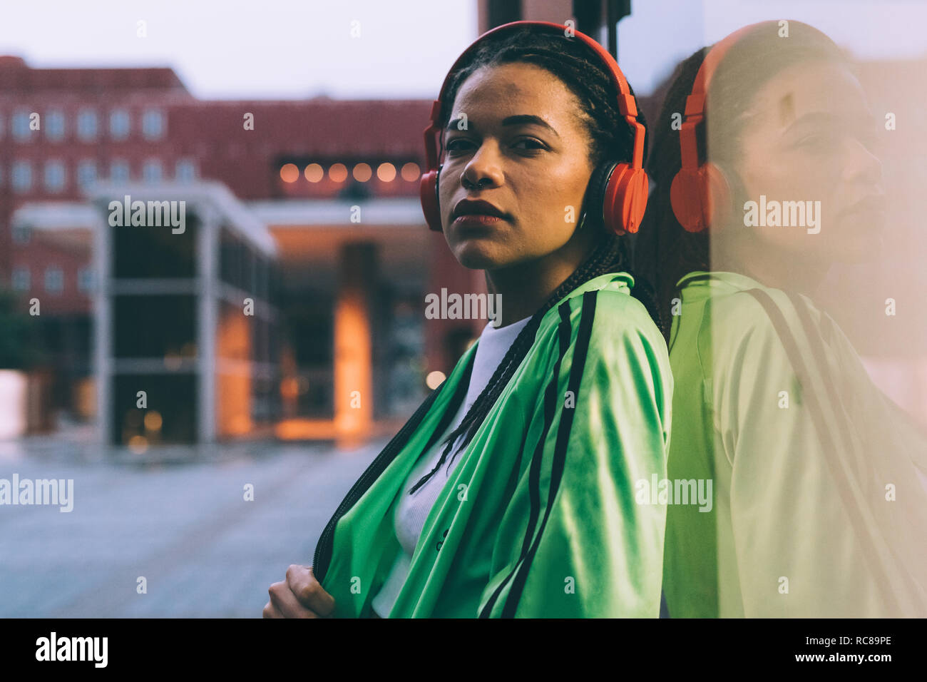 Woman with headphones leaning against glass window, Milan, Italy Stock Photo