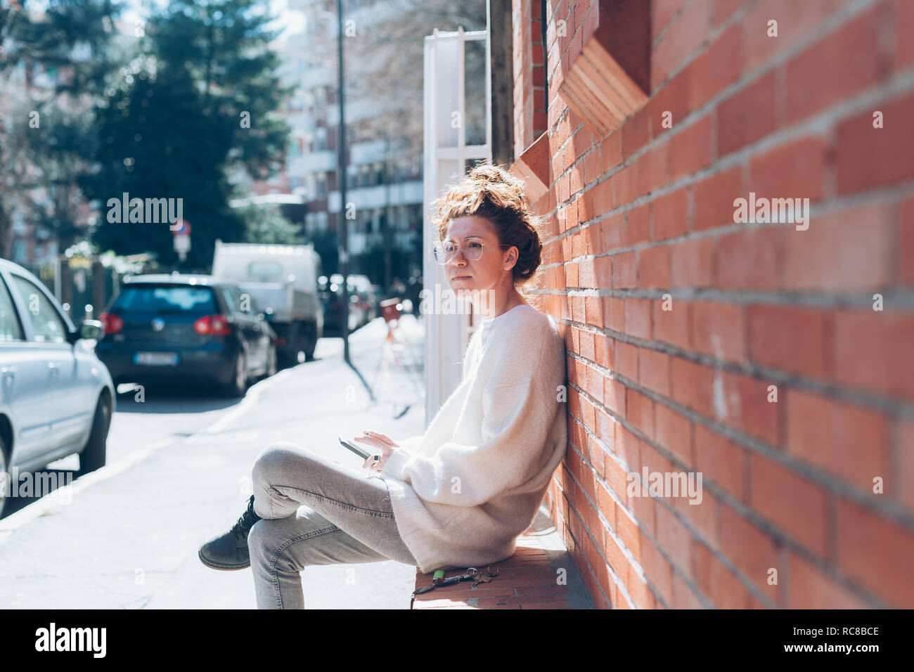 Woman with cellphone on bench on sunny street, Milan, Italy Stock Photo