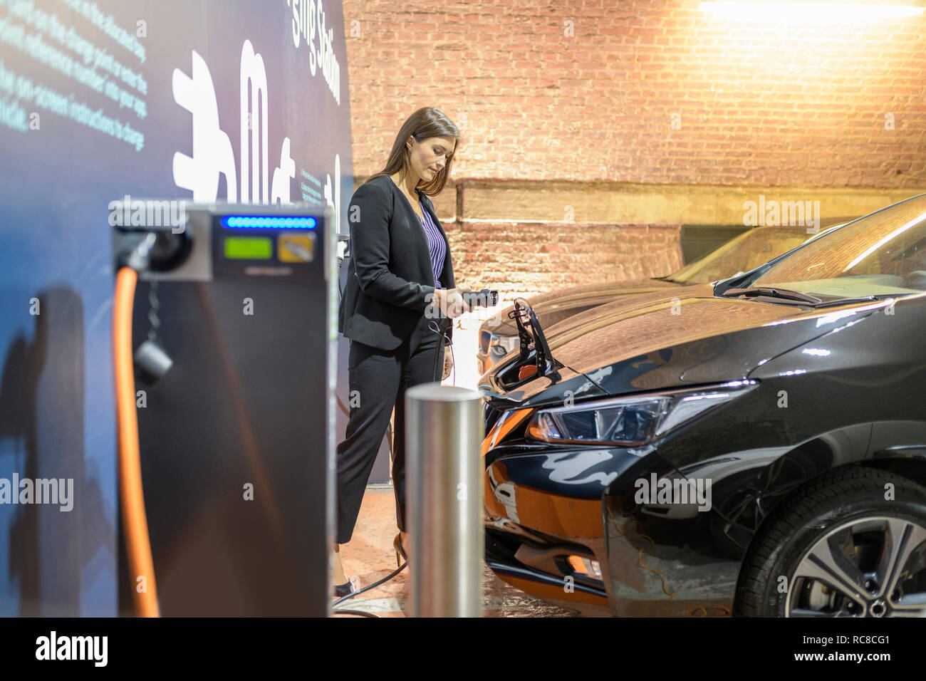 Businesswoman plugging in car at electric vehicle charging station, Manchester, UK Stock Photo
