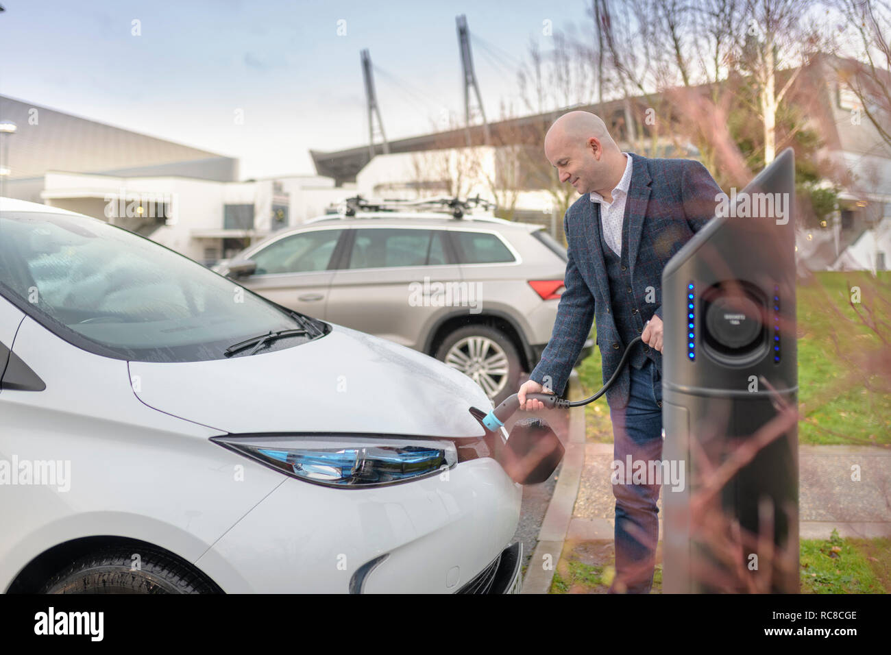 Businessman plugging in electric car at charging point, Manchester, UK Stock Photo