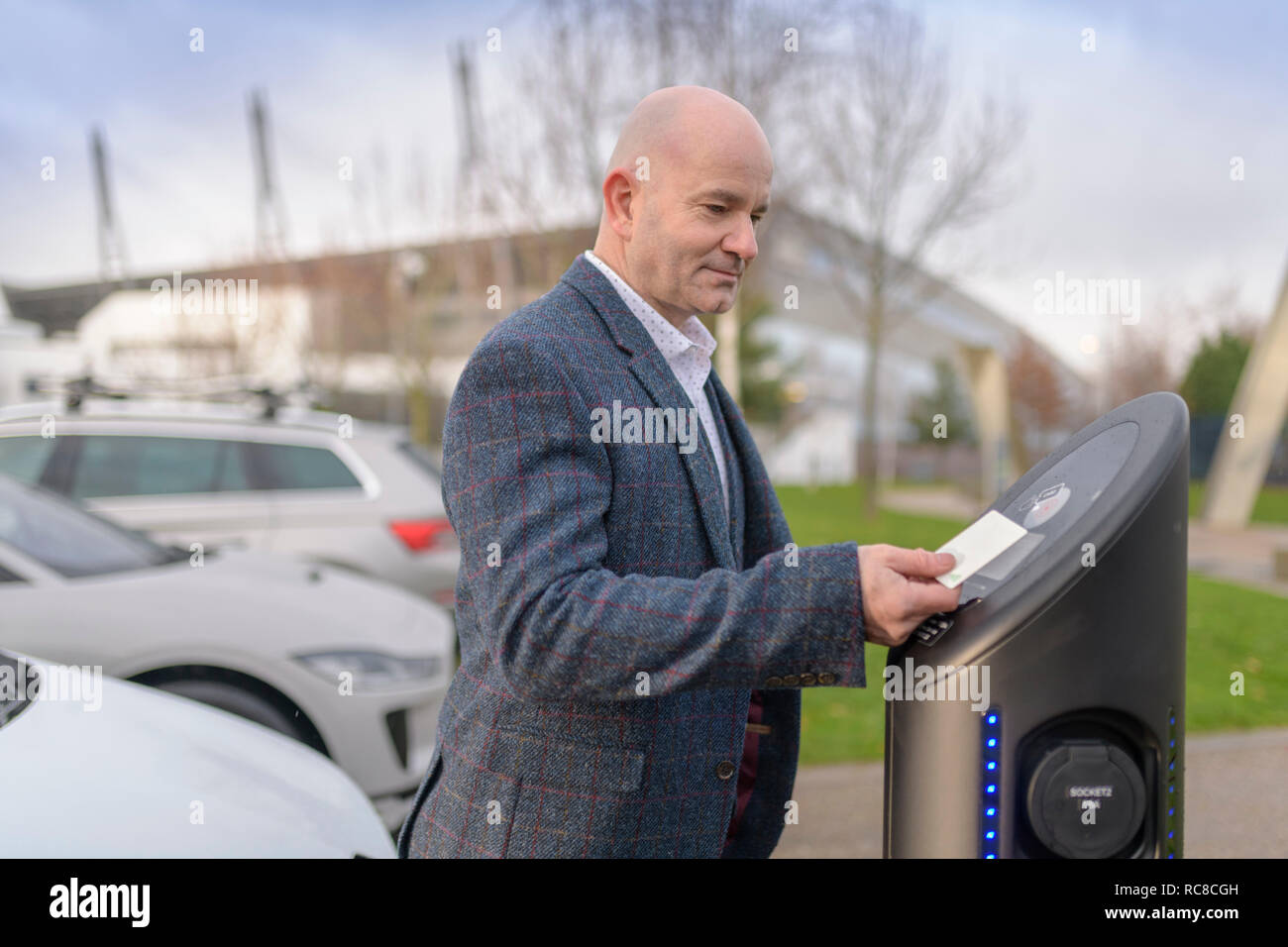 Businessman using access card at electric car charging point, Manchester, UK Stock Photo