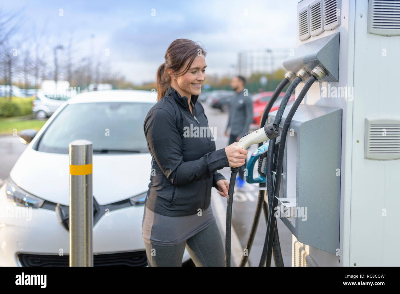 Sportswoman at electric car charging point, Manchester, UK Stock Photo