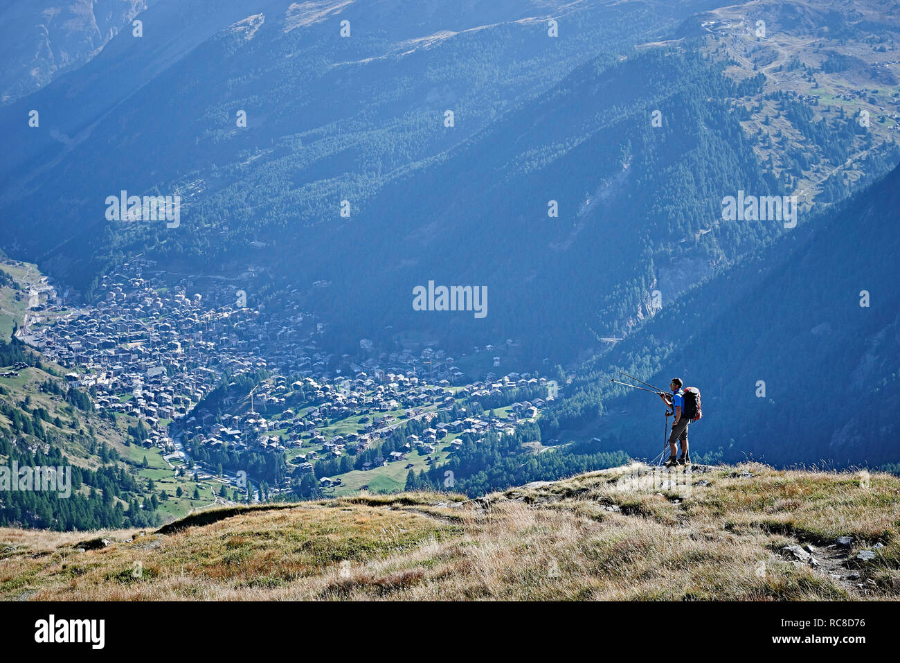 Hiker on grassy cliff overlooking valley, Mont Cervin, Matterhorn, Valais, Switzerland Stock Photo