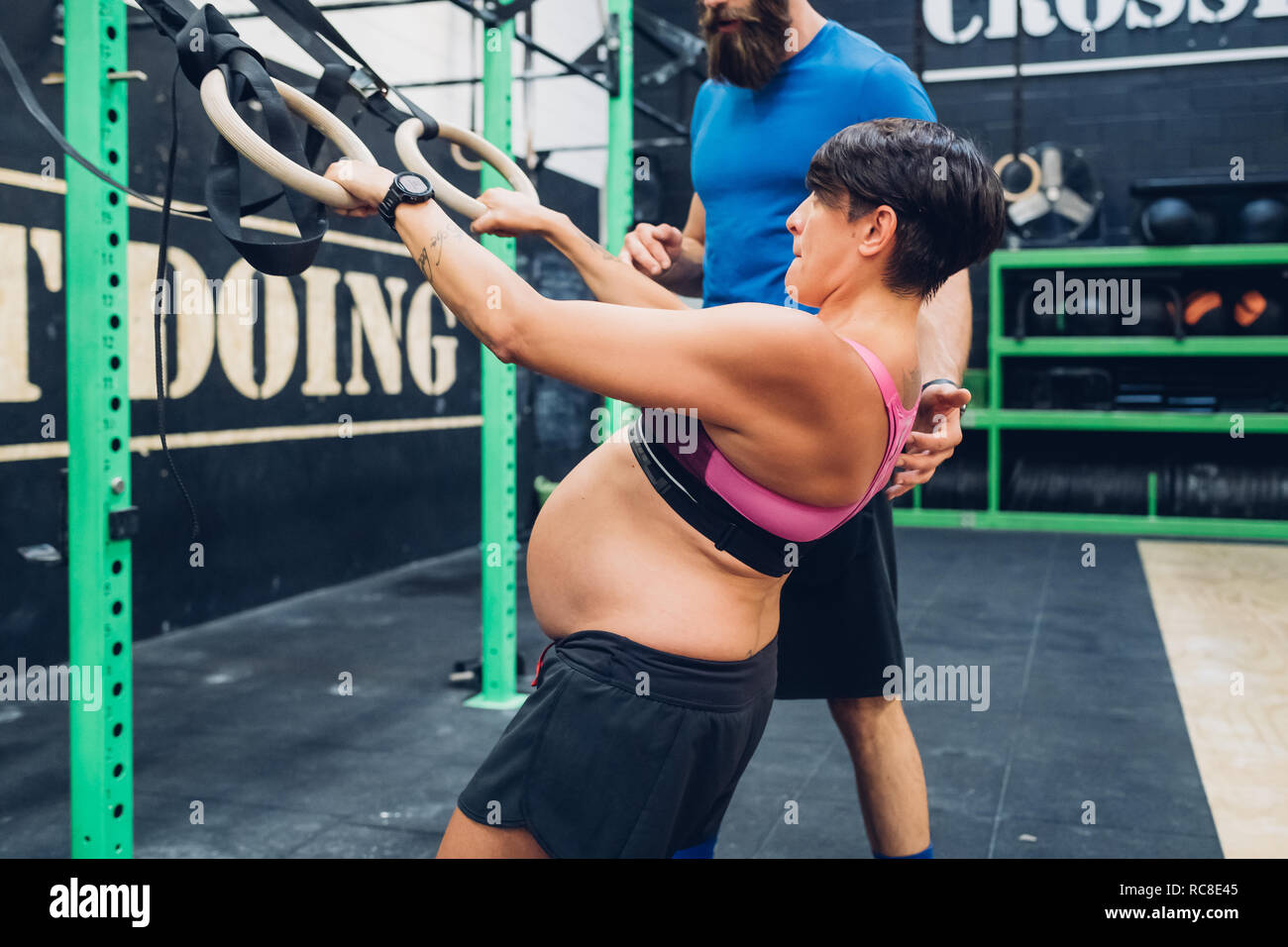 Trainer guiding pregnant woman using exercise equipment in gym Stock
