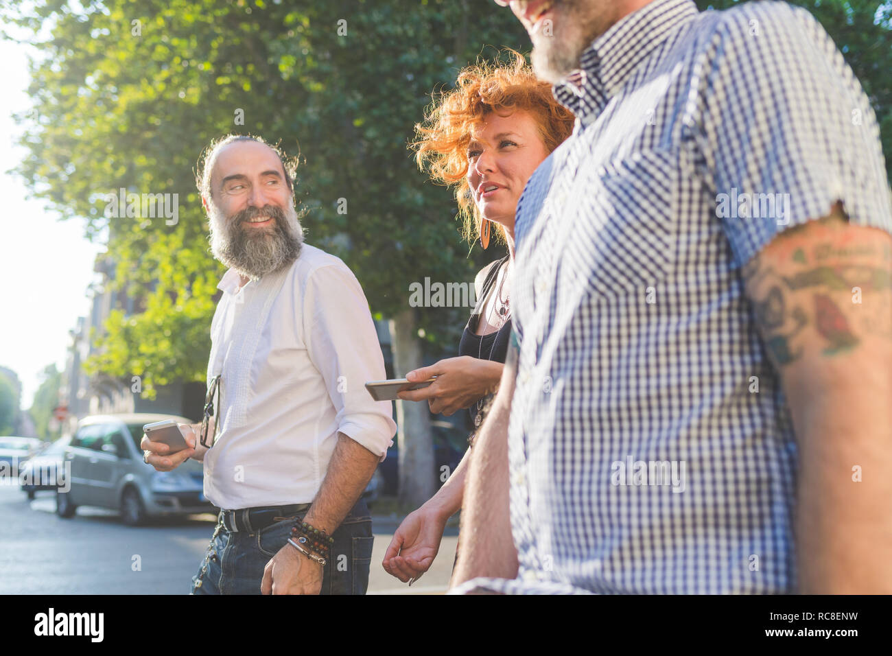 Mid adult woman and male friends chatting while strolling on city street Stock Photo