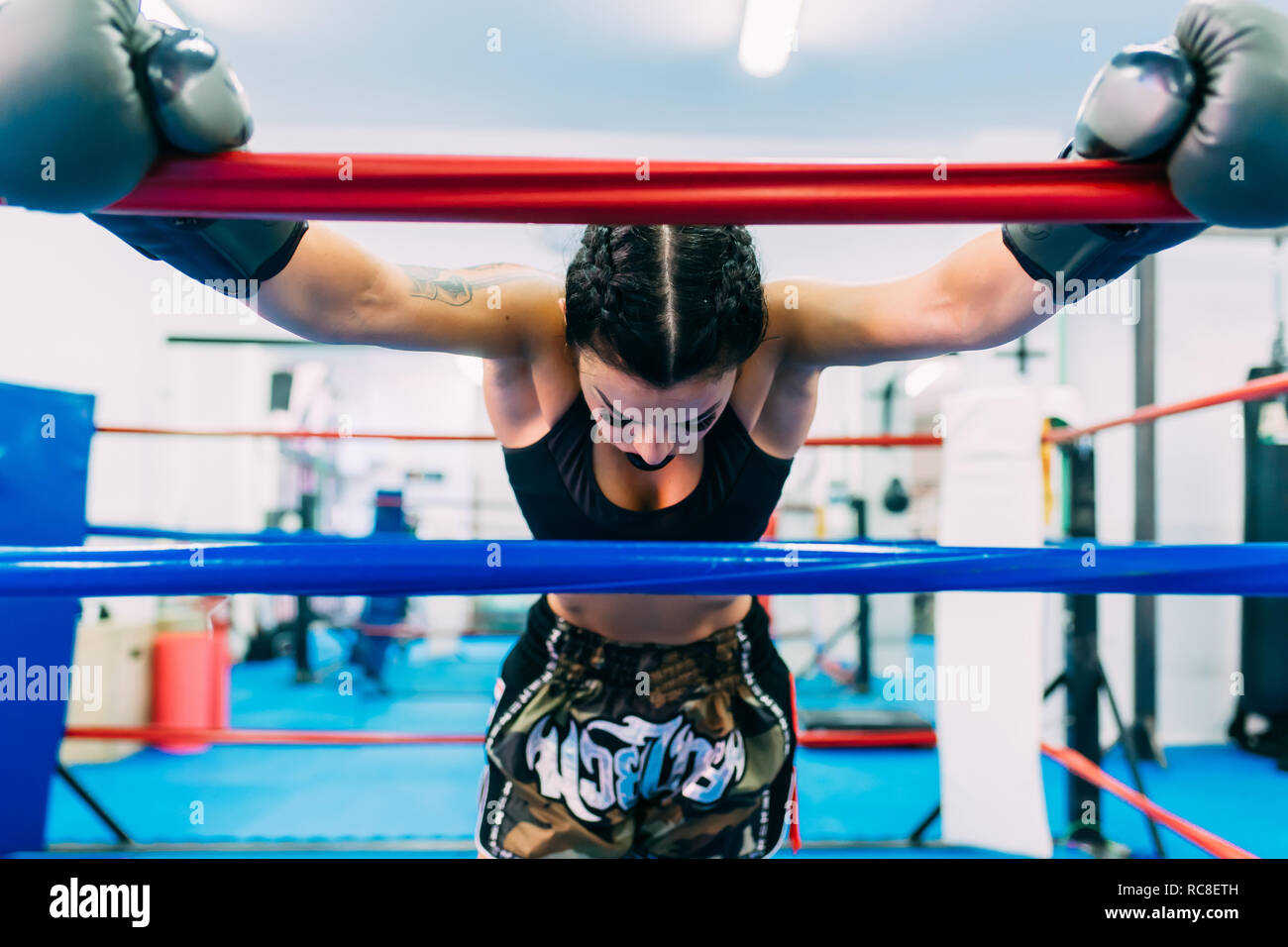 Exhausted female boxer leaning over boxing ring ropes Stock Photo