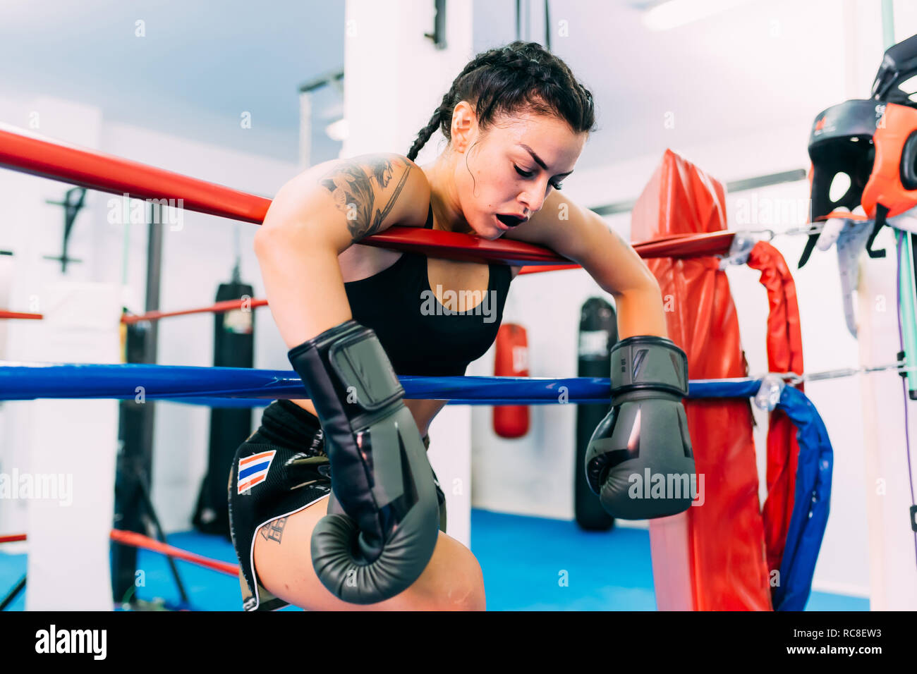 Exhausted female boxer leaning over boxing ring ropes Stock Photo