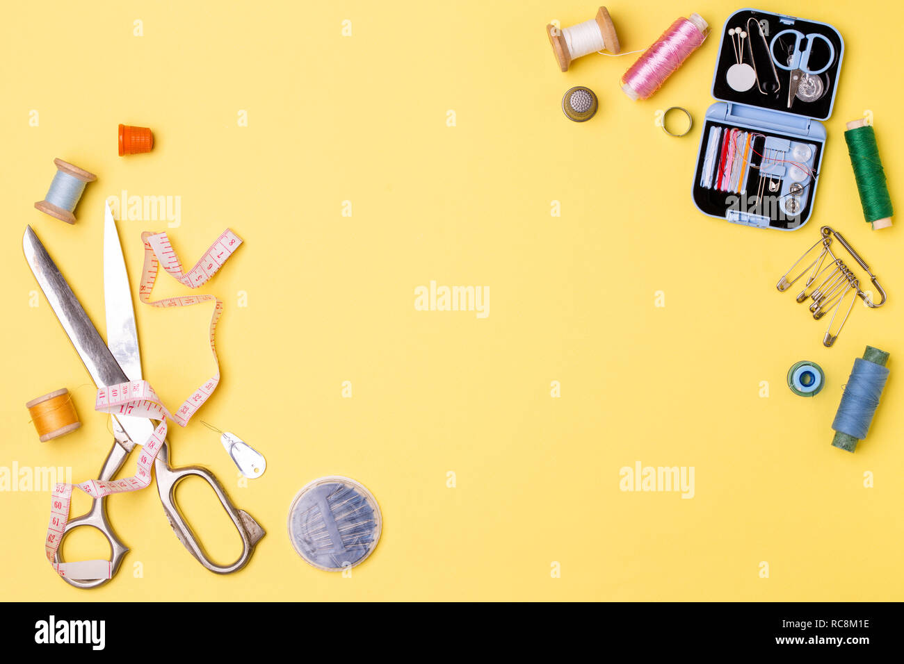 Composition with threads and sewing accessories - scissors, centimeter, pins on yellow background. Stock Photo